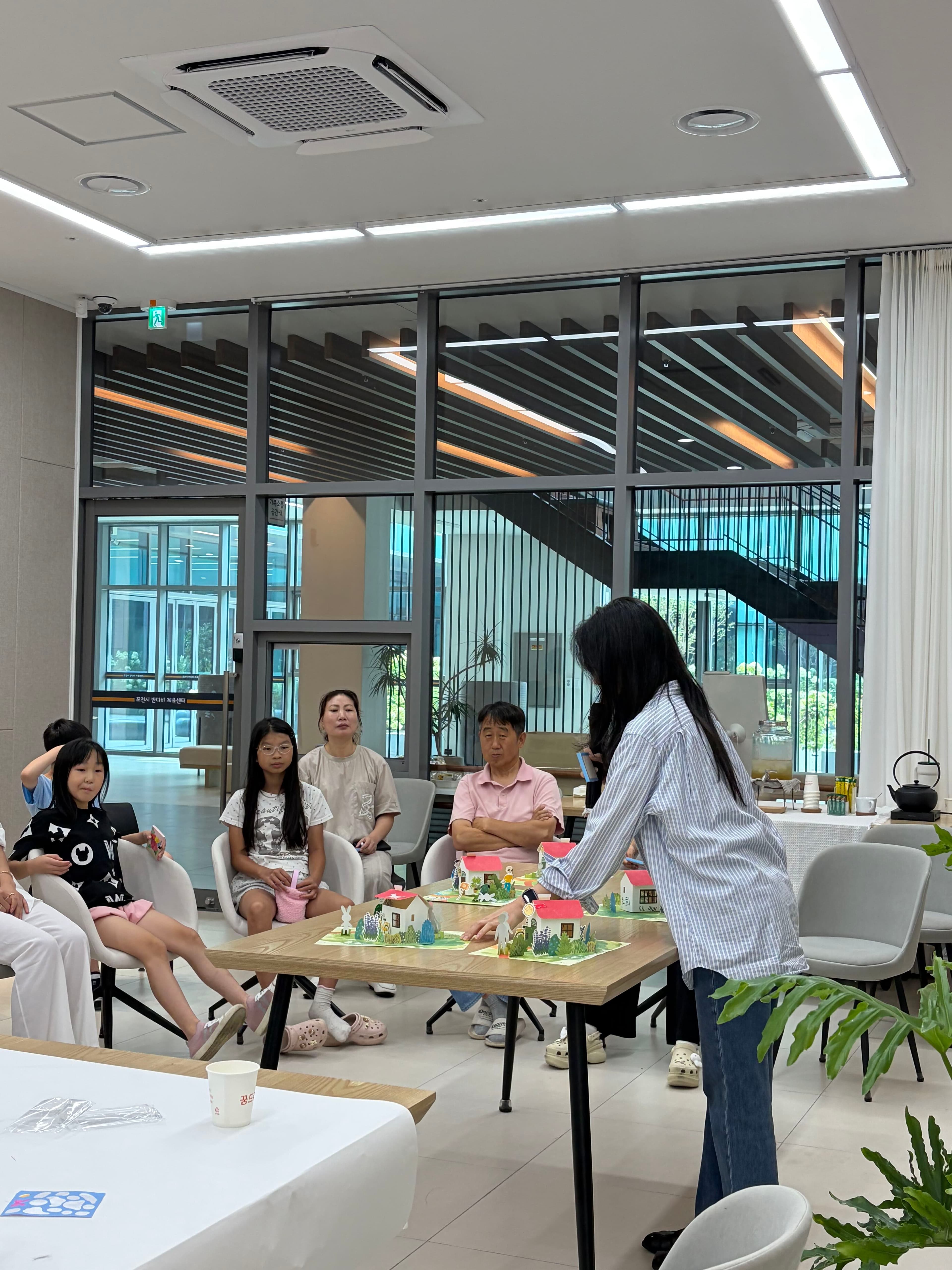 진행자와 가족들이 둘러앉아 팝업 크래프트를 함께 만드는 모습